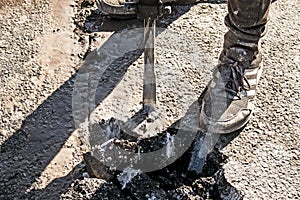 A worker repairs the road surface with a jackhammer on a summer day