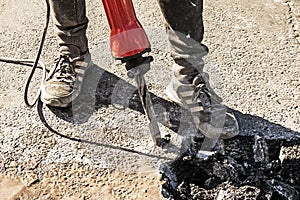 A worker repairs the road surface with a jackhammer on a summer day