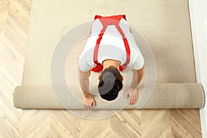 Worker rolling out new carpet flooring indoors, top view