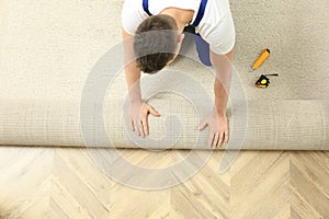 Worker rolling out new carpet flooring indoors, top view