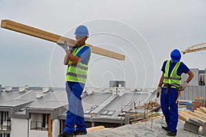 A worker on the roof carries a beam while other worker in the background place a hammer stock image