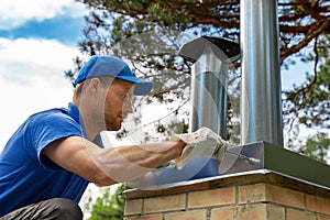 Worker on the roof installing tin cap on the brick chimney