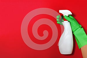 Worker`s hand in a rubber green protective glove with a spray bottle on a red color background. The concept of cleaning, home car