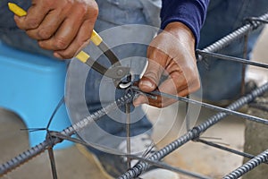 Worker`s hand tying reinforcing steel bars, tightening wire on rebar using a pincers for formwork construction