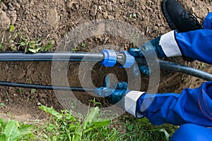 Worker`s hands hold a black pipe over a dug hole in the ground