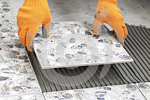 Worker`s hands hold a tile and place it on floor smeared with glue. Process of laying ceramic tiles.