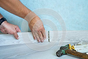 Worker`s hands Instal plastic skirting board on laminate flooring. Renovation of baseboard at home.