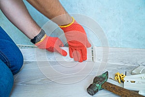 Worker`s hands Instal plastic skirting board on laminate flooring. Renovation of baseboard at home.