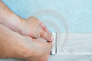 Worker`s hands Instal plastic skirting board on laminate flooring. Renovation of baseboard at home