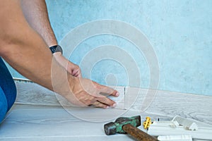 Worker`s hands Instal plastic skirting board on laminate flooring. Renovation of baseboard at home.