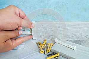 Worker`s hands Instal plastic skirting board on laminate flooring. Renovation of baseboard at home.