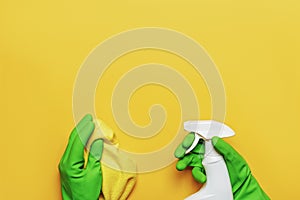 Worker`s hands in rubber protective gloves with a napkin and a spray bottle on a yellow background.