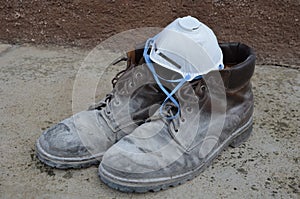 Worker`s shoes dirty from all-day work construction dust on leather boots on concrete with mask protecting lungs from dust