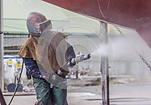 Worker, sandblasting the corrode hull of a sailing vessel