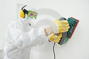 Worker with sander at wall filling photo