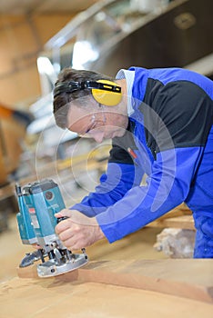 Worker sanding wood for luxury yachts in boatyard