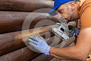 Worker sanding a wooden window shutters on house exterior