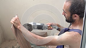 Worker sawing tiles with an angle grinder. A man makes repairs and saws tiles