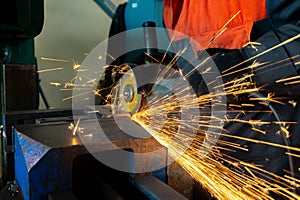 A worker saws a metal blank with a cutting wheel with a grinding machine, large sparks fly around