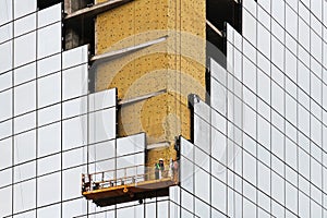 Worker on the scaffold elevator evens insulation boards at the corner of building