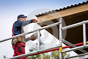 Man on scaffolding painting house roof planks with paint roller