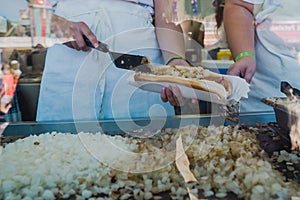 Worker scoops grilled onions onto a footlong hotdog while working in a booth at a fair