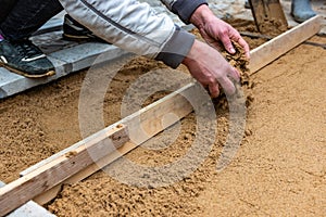 Worker screeding sand bedding to level for laying paving slabs.