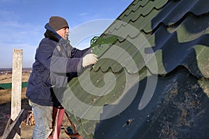 The worker screws the snow retaining elements to the roof with a screwdriver