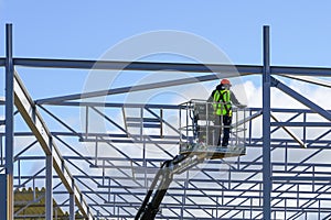 Worker in self propelled boom lift basket in uniform on a building steel framework background