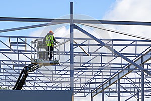 Worker in self propelled mobile crane basket in uniform on a building steel framework background