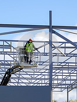 Worker in self propelled mobile crane basket in uniform on a building steel framework background