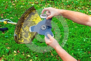 The worker sets the knife into the trimmer or lawnmower that lies on the grass before haymaking