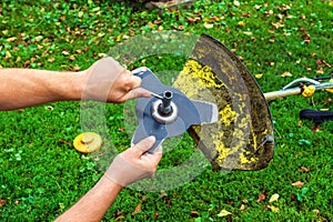 Worker sets the knife into the trimmer or lawnmower that lies on the grass before haymaking