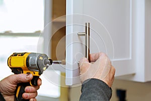 The worker sets a new handle on the white cabinet with a screwdriver