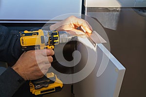 Worker sets a new handle on the white cabinet with a screwdriver installing kitchen cabinets