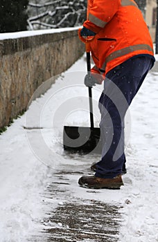 Worker while shoveling snow from frozen sidewalk