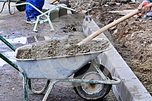 Worker shovels concrete from a wheelbarrow at curb block installation.