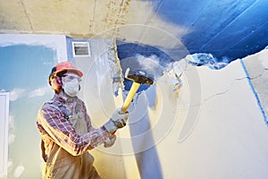 Worker with sledgehammer at indoor wall destroying