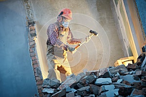 Worker with sledgehammer at indoor wall destroying