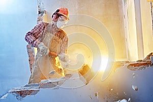 Worker with sledgehammer at indoor wall destroying