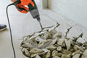 Worker smashes concrete floor with electric hammer drill