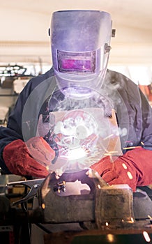 Worker in special clothes and helmet works as welding machine in his workshop