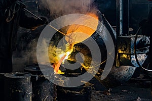 A worker with a special tool stirs the molten metal in a casting ladle