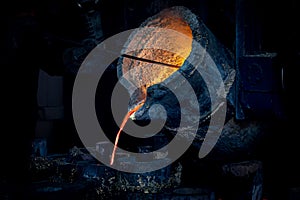 A worker with a special tool stirs the molten metal in a casting ladle