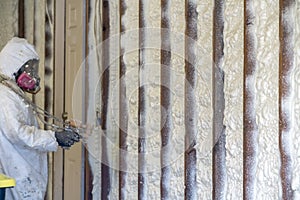 Worker spraying closed cell spray foam insulation on a home