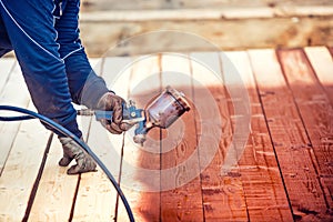 Worker spraying paint over timber wood. Construction worker with spray gun