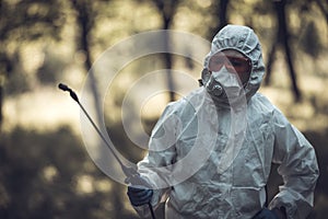 A worker sprays pesticides on trees outdoors. Tree pest control