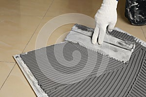 Worker spreading concrete over ceramic tile with spatula on floor, closeup