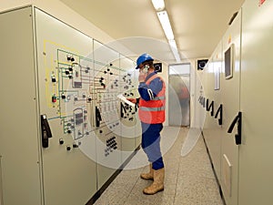 Worker stay in large control room. Power Plant Control Panels with schema. Engineer standing in front of the control panel