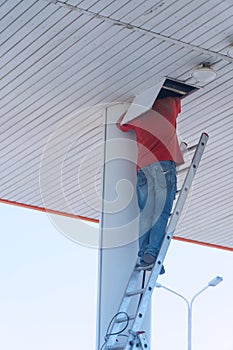 Worker on a stepladder checks or repairs something in a hatch on the ceiling